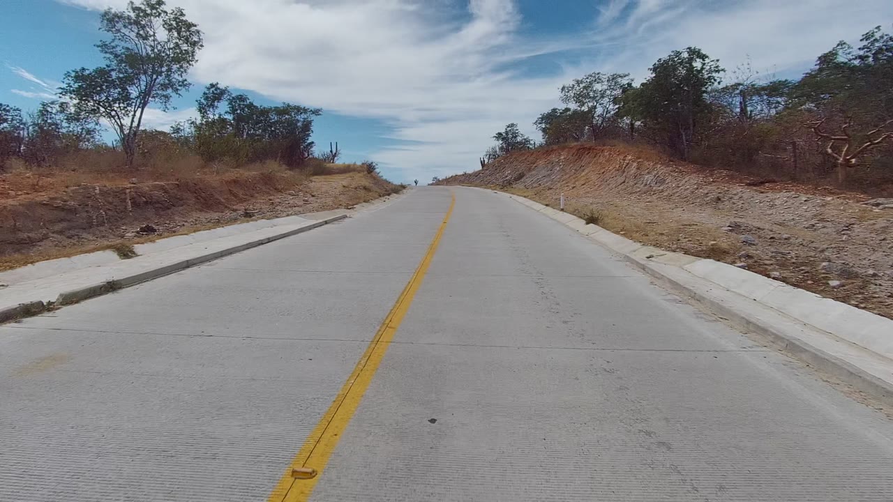 Yellow center line leading up a paved road past scrubby hills.