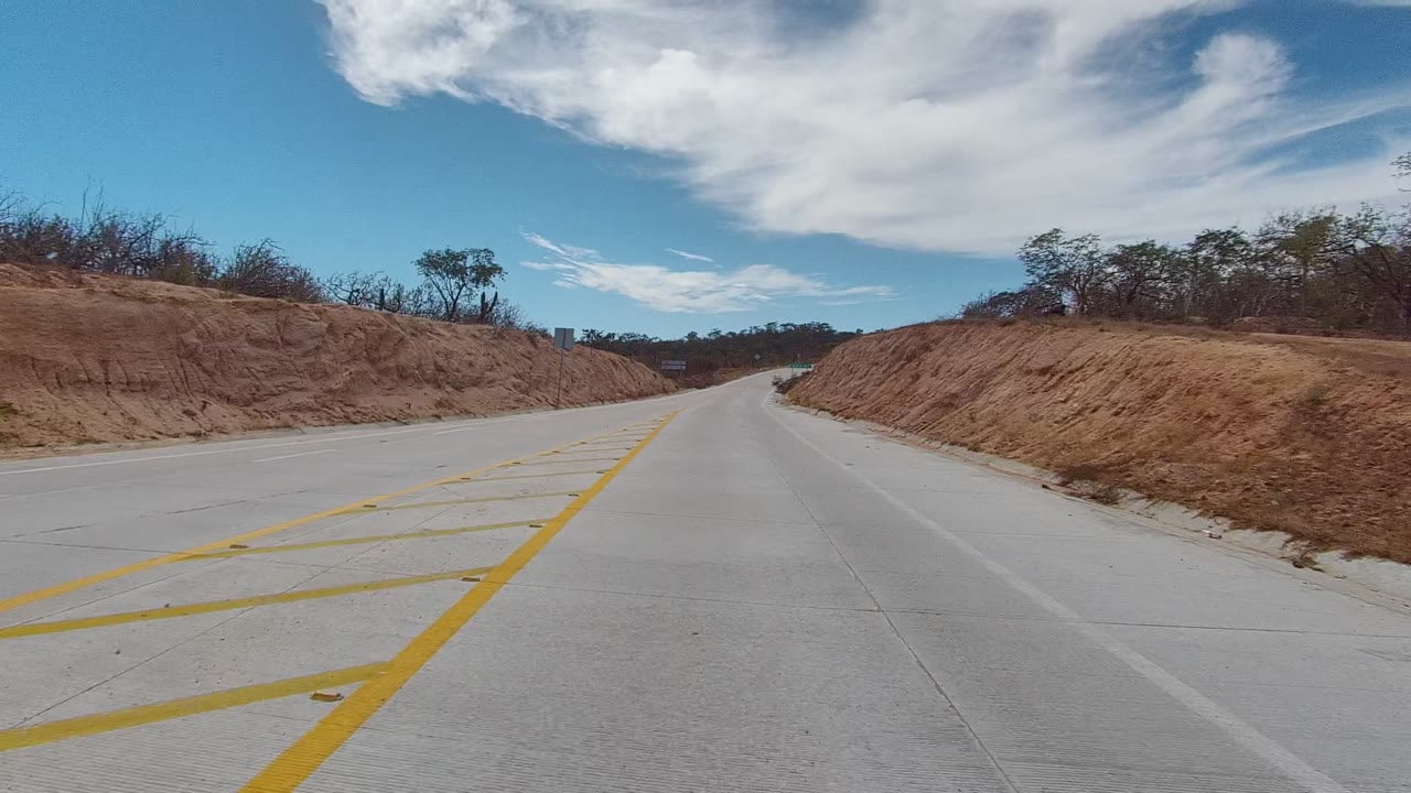 Road with yellow markings between dry red soil banks.