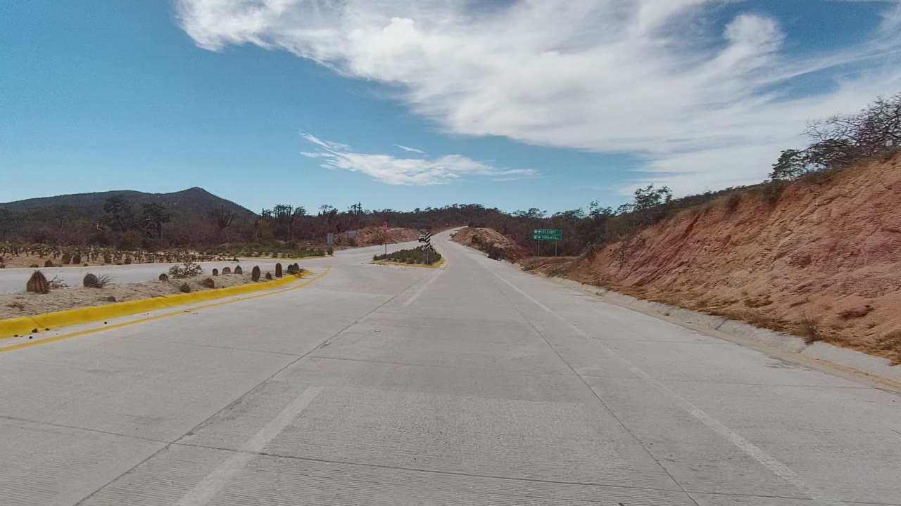 Road approaching a desert intersection with cacti, signs, and hills