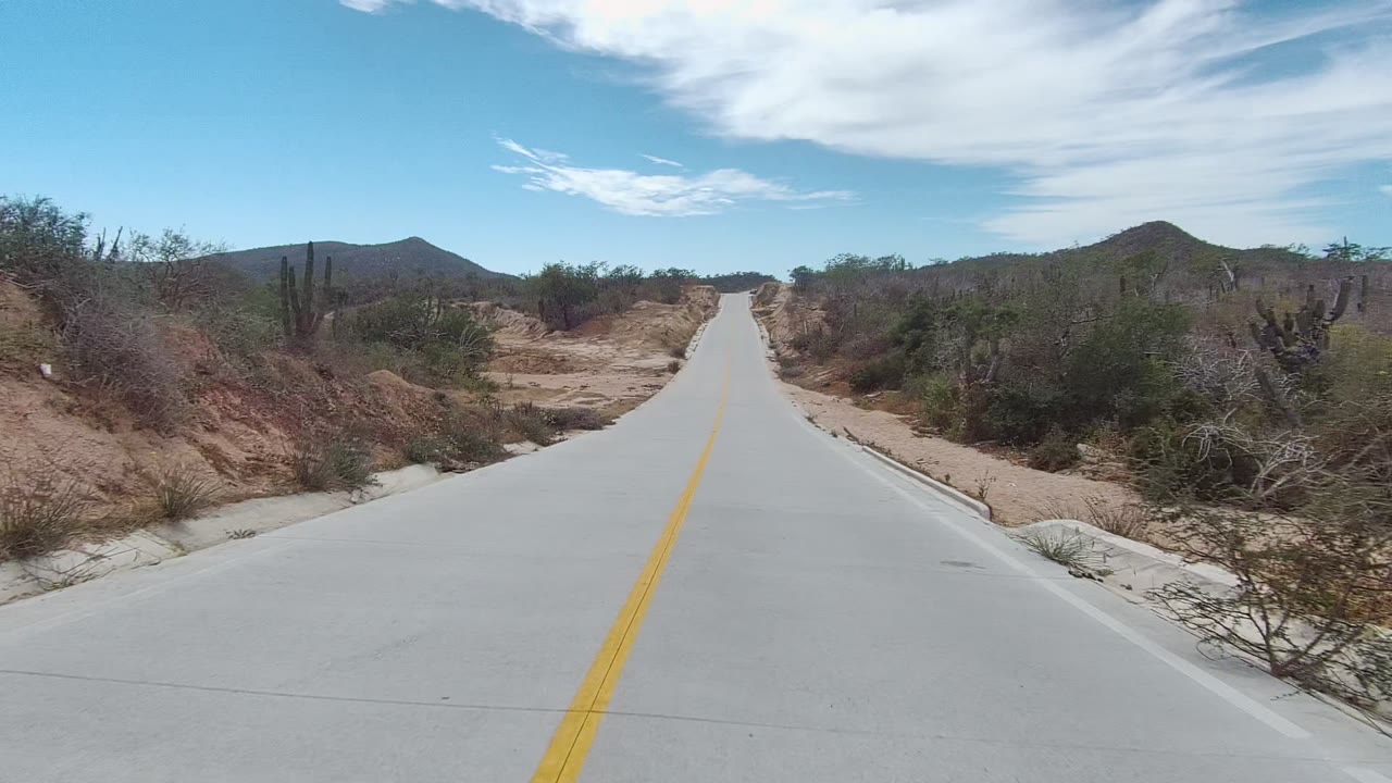 Two seconds in, the road opens toward low hills with cactus and scrub on both sides of the East Cape Los Cabos roadside, and no visible people.