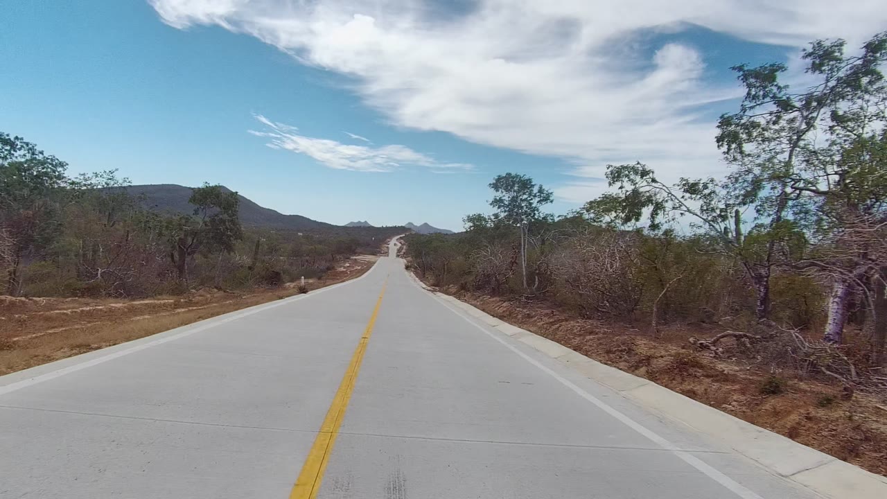 Two-lane road with yellow line, dry vegetation, and low mountains.