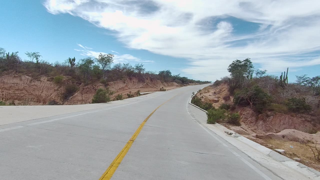Empty paved road climbing between arid banks and sparse vegetation