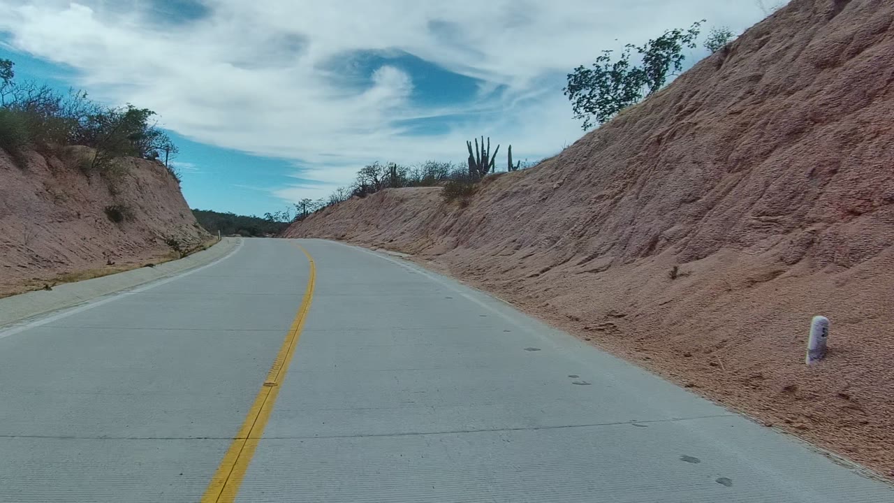Curving paved road with yellow center line beside arid hills