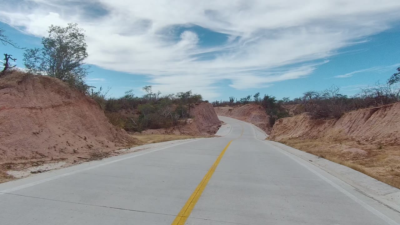 Road curves between cut banks of dry reddish soil.