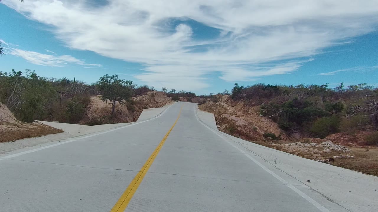 Road curving gently through brown hills with scrub on both sides.