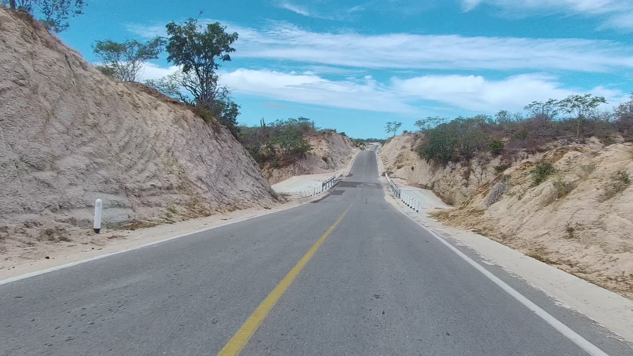 Two-lane road approaching a small guardrail section in dry terrain