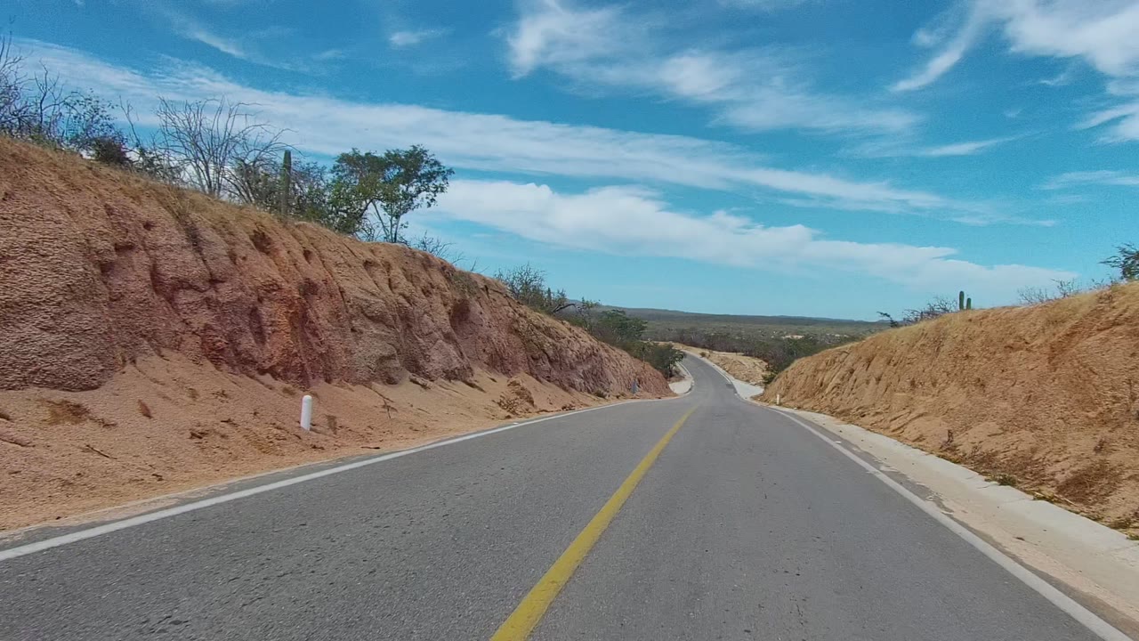 Road curves through dry hills with sparse roadside vegetation