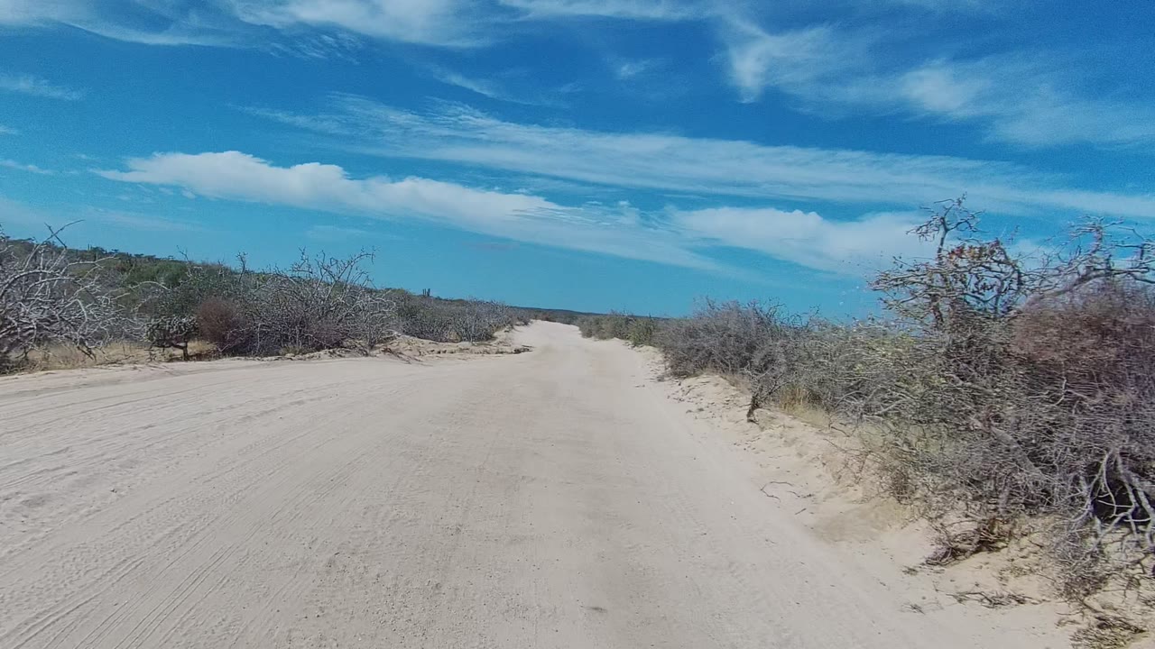 Two seconds in, the sandy East Cape Los Cabos track widens slightly, with low shrubs on both sides and no visible people.