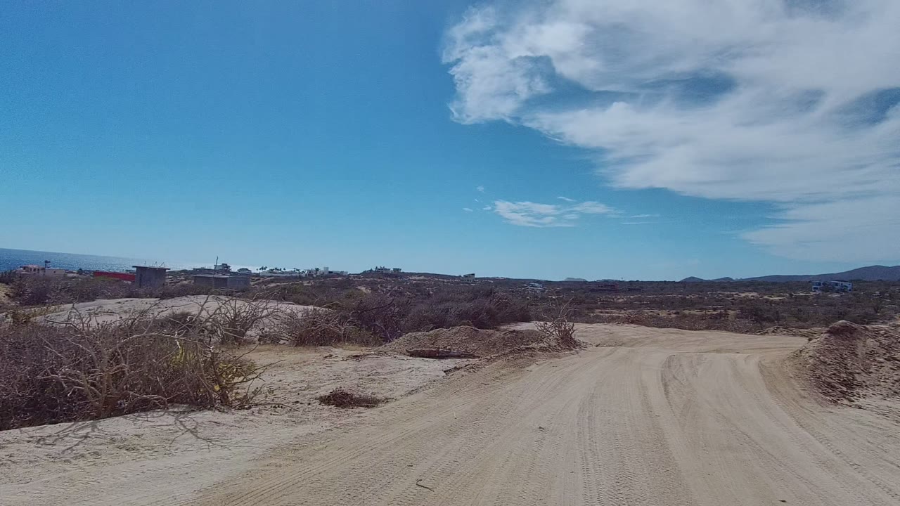 Dusty road ahead with dry brush and distant hills