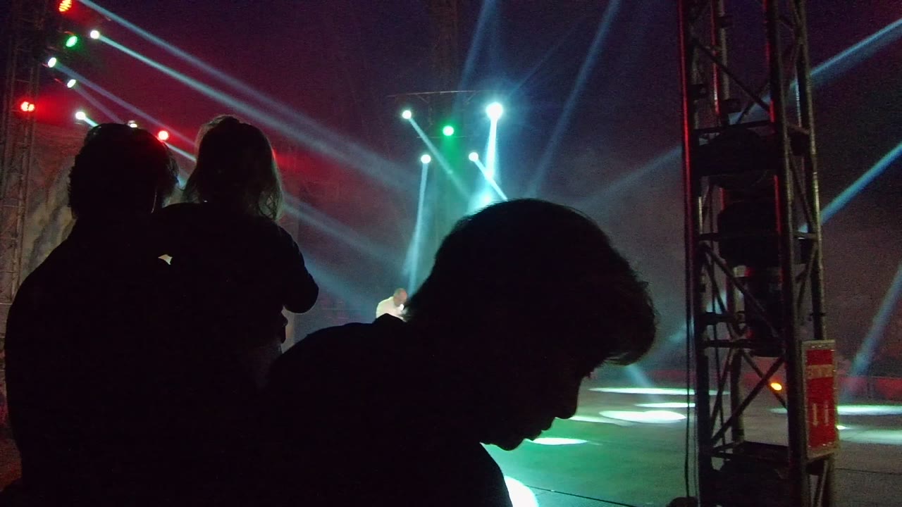 Dark foreground spectators beside a stage truss and colored spotlights