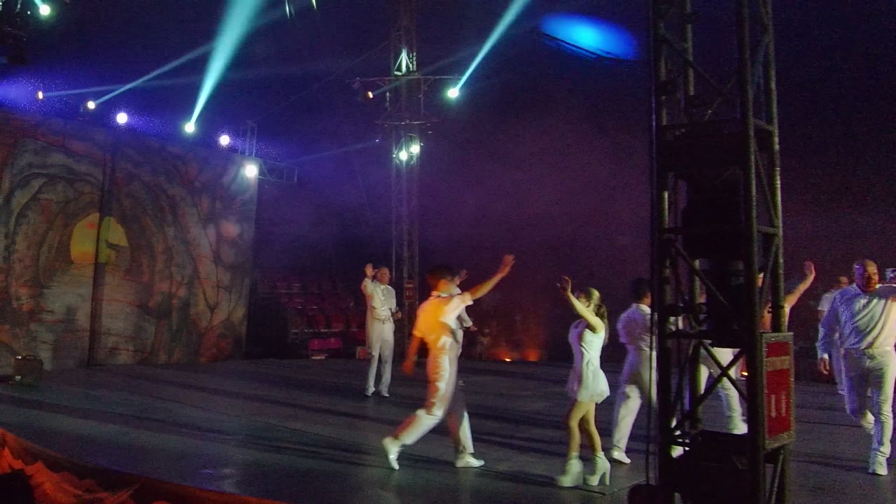 Dancers cross a lit stage with a decorative backdrop behind them.