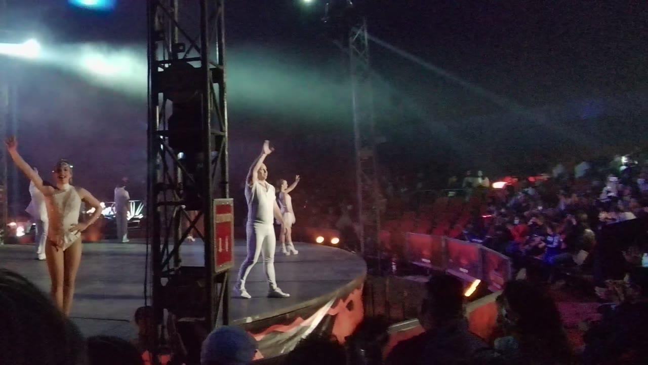 Several white-costumed performers gesture across the stage as blue and white spotlights cut through haze over the audience in San Jose Del Cabo, Mexico.