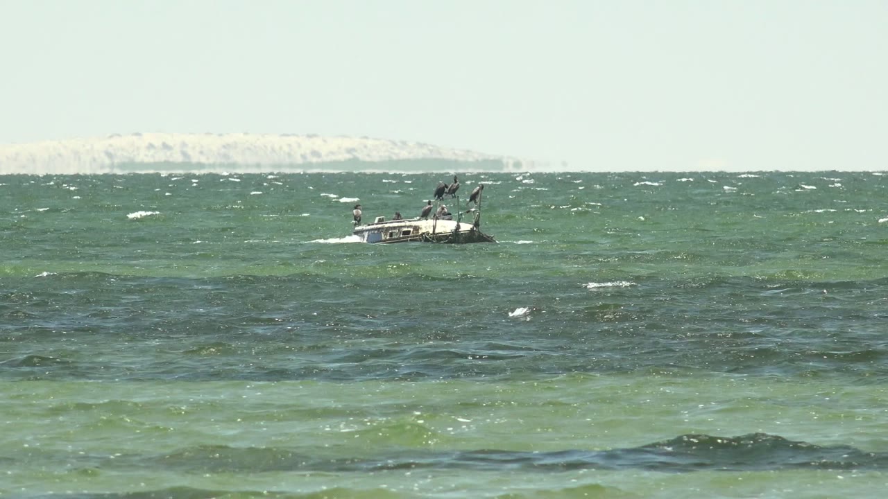 Small boat nearer the center of a choppy ocean with whitecaps.
