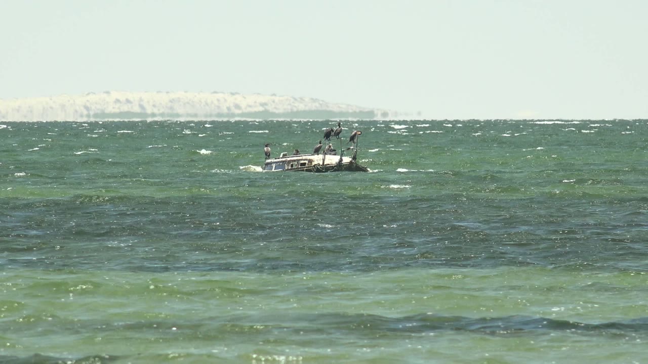 A small boat with people aboard rides right of center on choppy San Carlos water, with a pale strip of distant shore across the upper background.