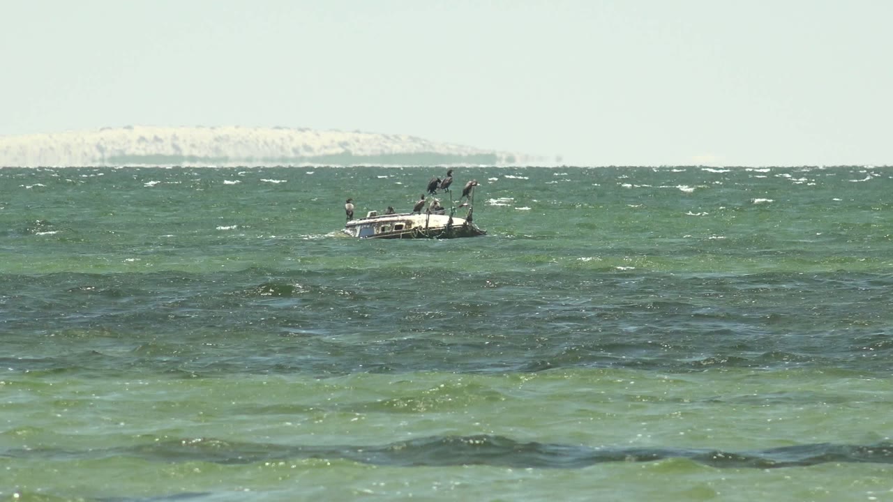 Small boat at left over green-blue sea with whitecaps and distant shore.