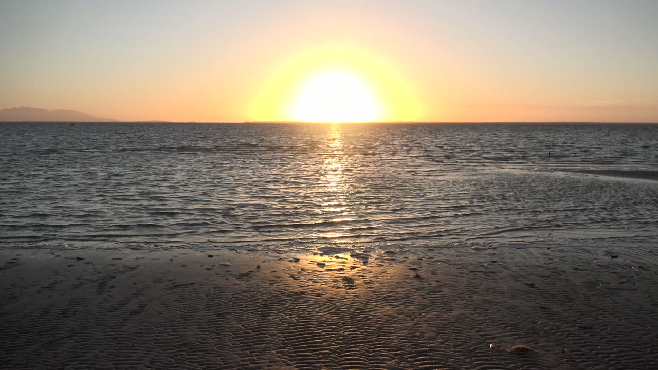 Sunset over the ocean in San Carlos, Baja California Sur, with gold reflection on wet sand and no visible people.
