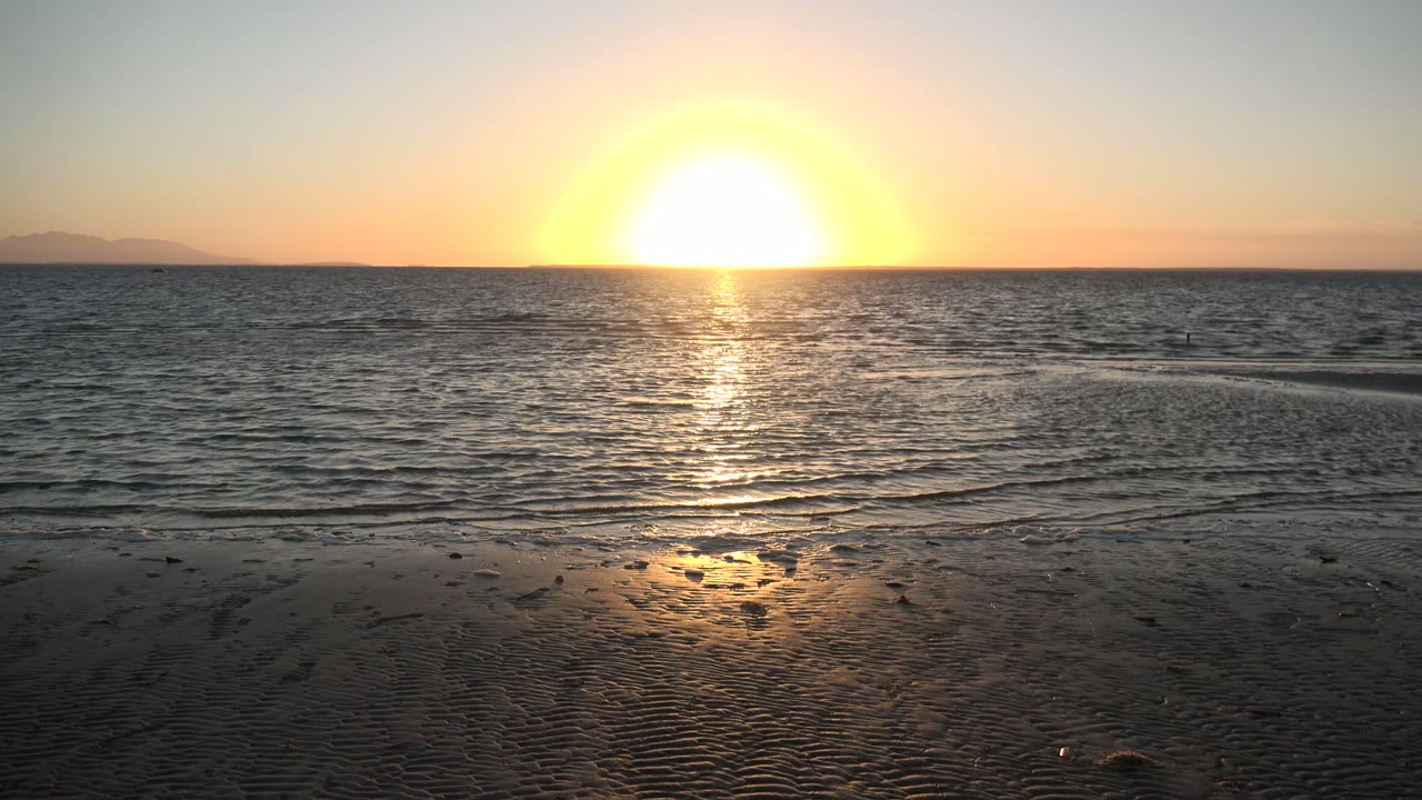 Low sun reflecting across rippled ocean and beach