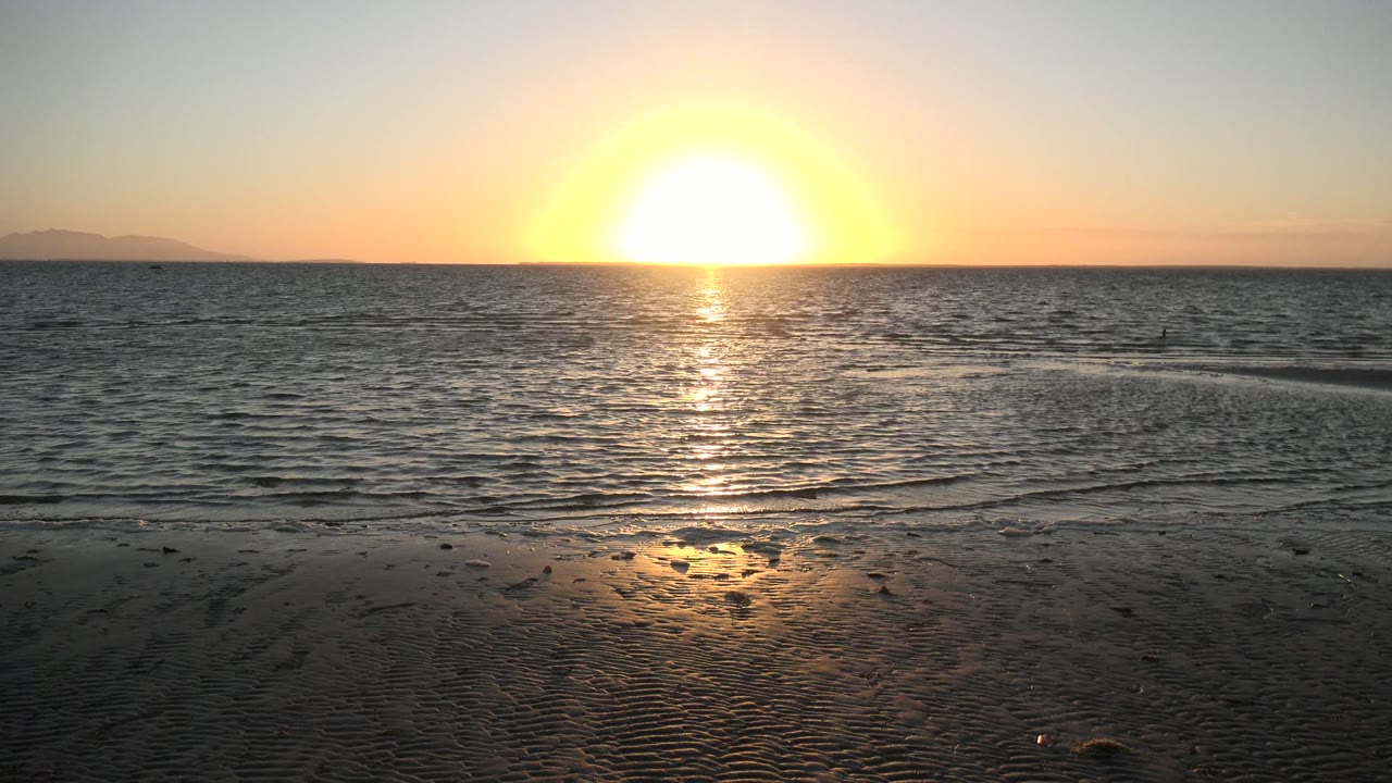 Golden sunset above gentle waves at San Carlos, Baja California Sur, with darker rippled sand in the foreground and no visible people.