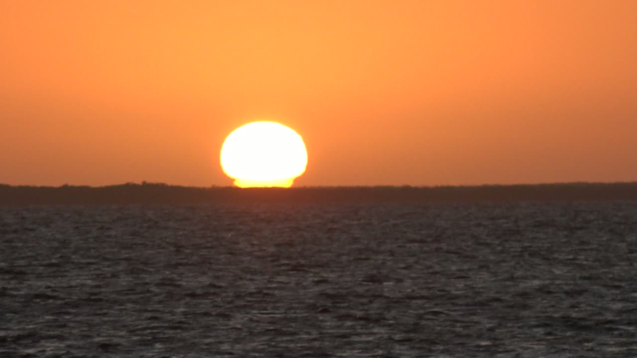At 0:02, the sun glows close to the distant land horizon while dark wave texture fills the lower frame in San Carlos, Baja California Sur, with no visible people.