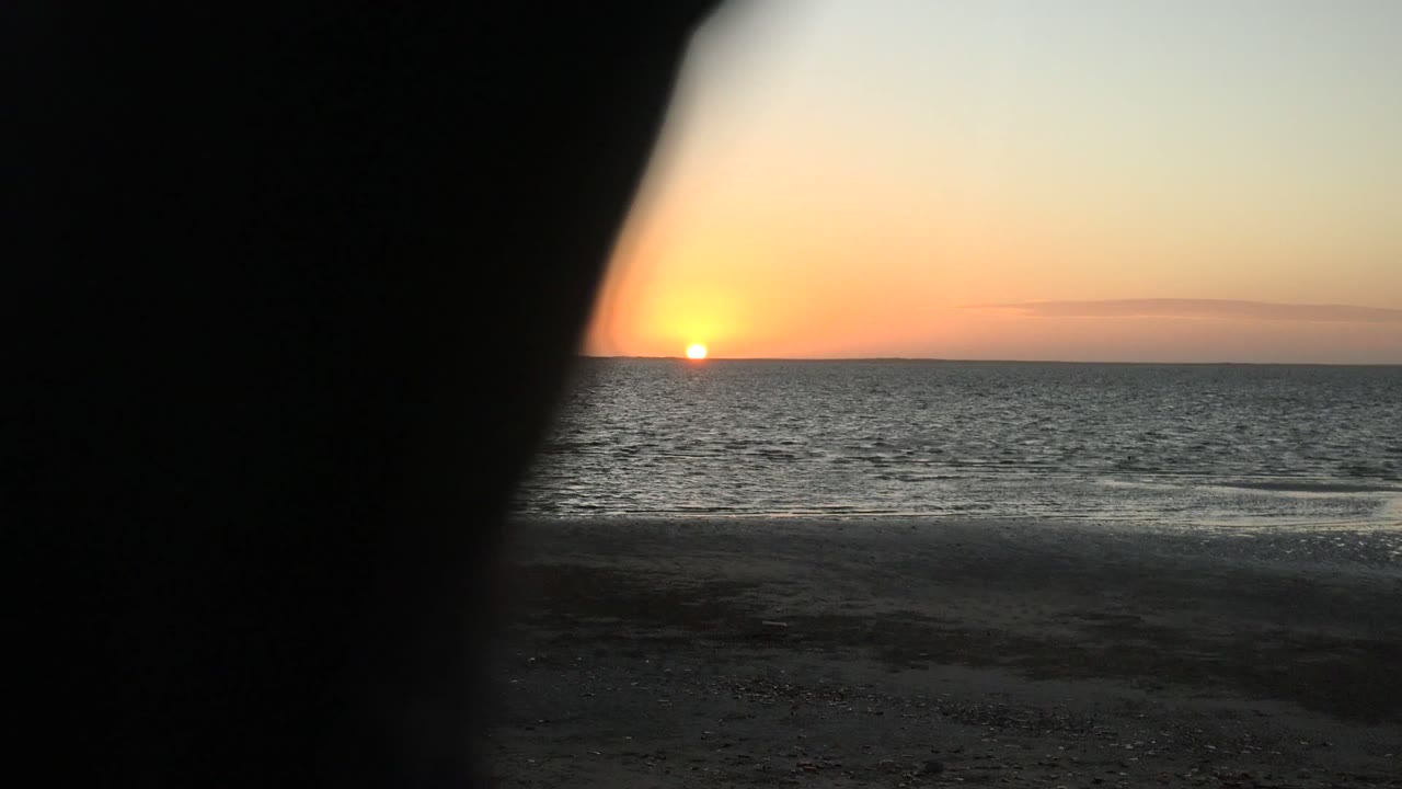 The San Carlos sunset remains visible over the ocean while a dark close foreground obstruction covers much of the center-right frame, with no visible people.