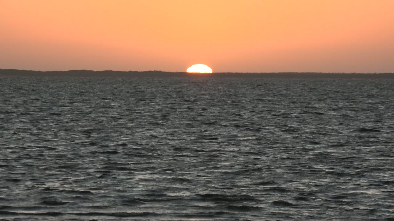 Low sun centered above dark ocean water
