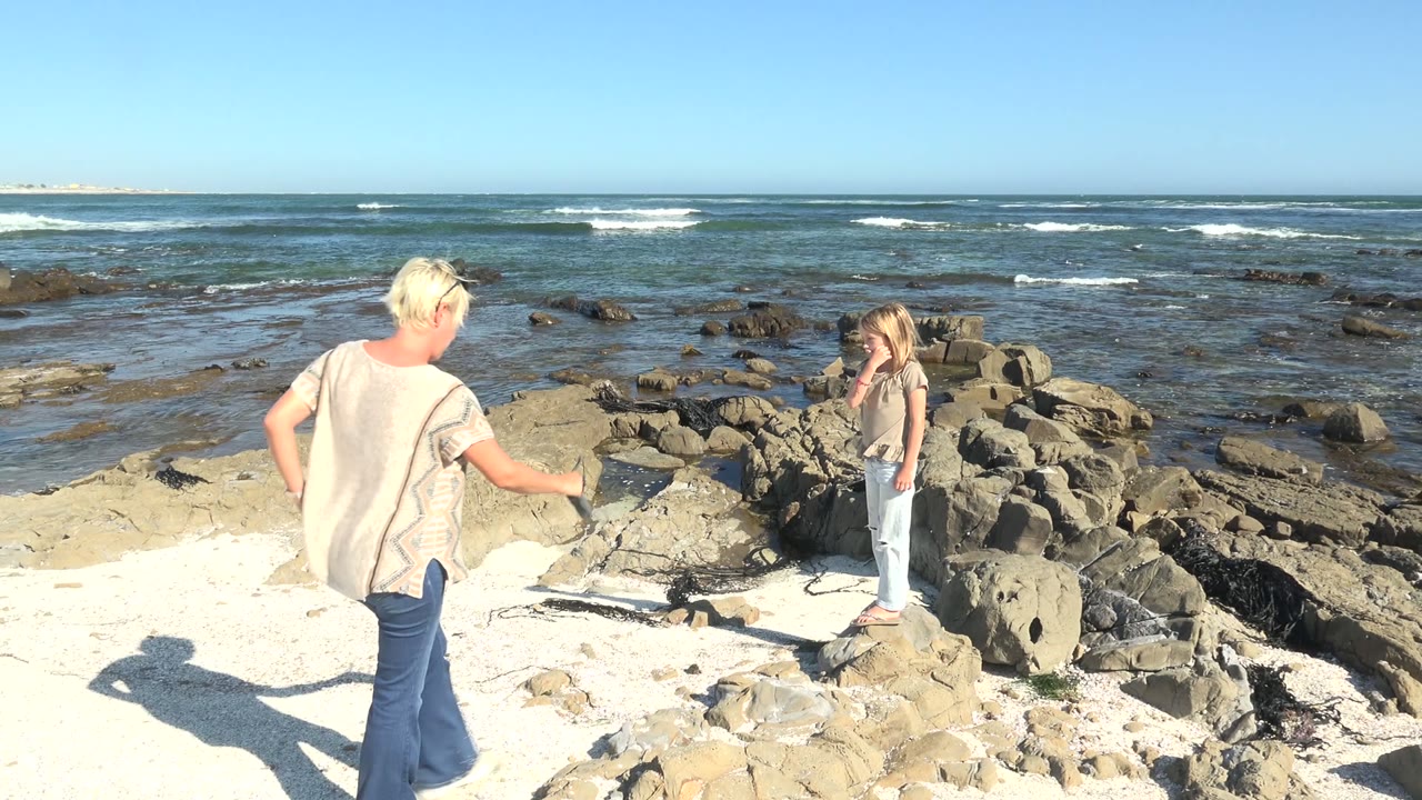 Adult walking toward child on rocks near low waves