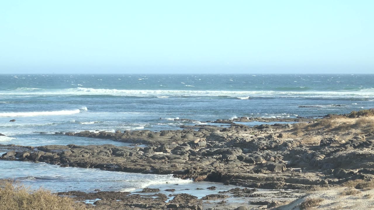 Blue ocean surf breaking behind dark coastal rocks.