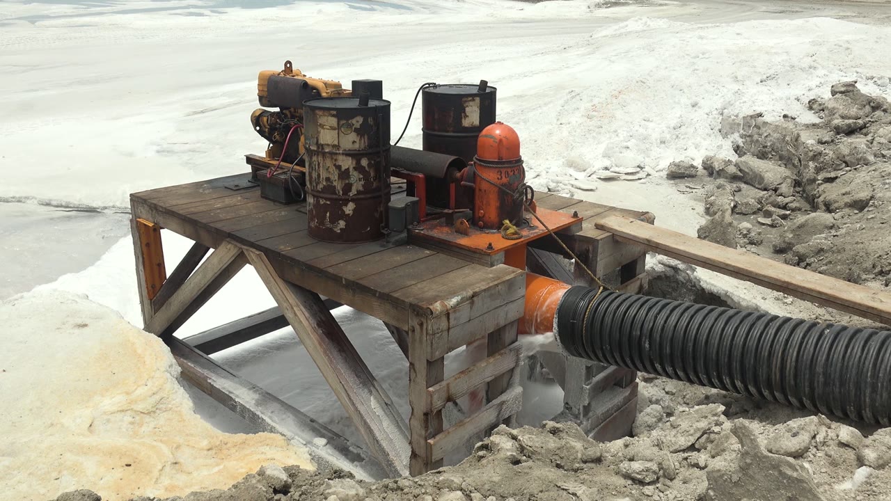 Industrial pump platform with black hose crossing pale slurry ground