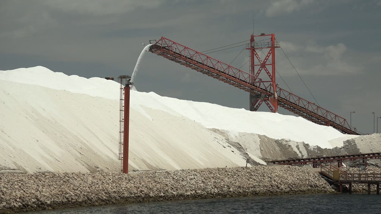 Red conveyor crossing white salt piles with water spraying from a tower.