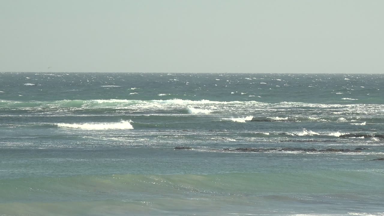 Wide view of ocean waves at La Bocana, Baja California Sur, with scattered whitecaps near the horizon, reef lines across the midground, and no visible people.