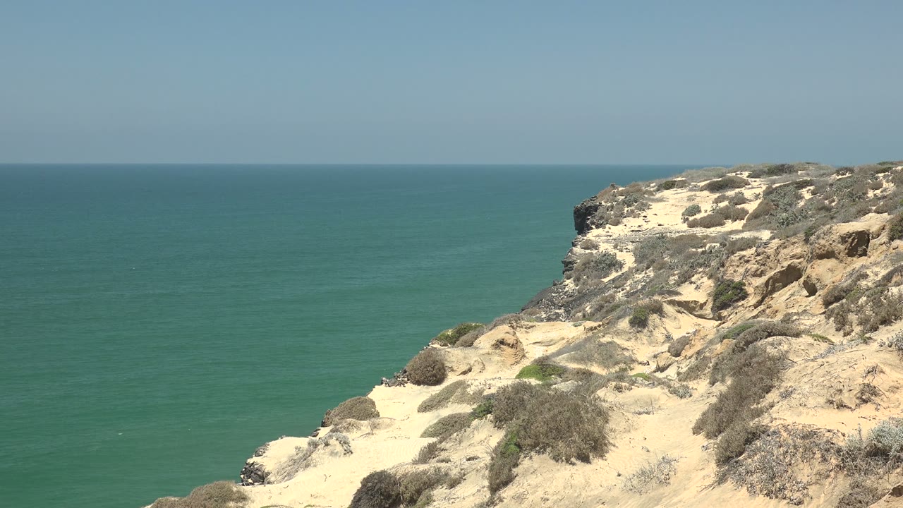 Rocky sandy bluff overlooking green-blue water.