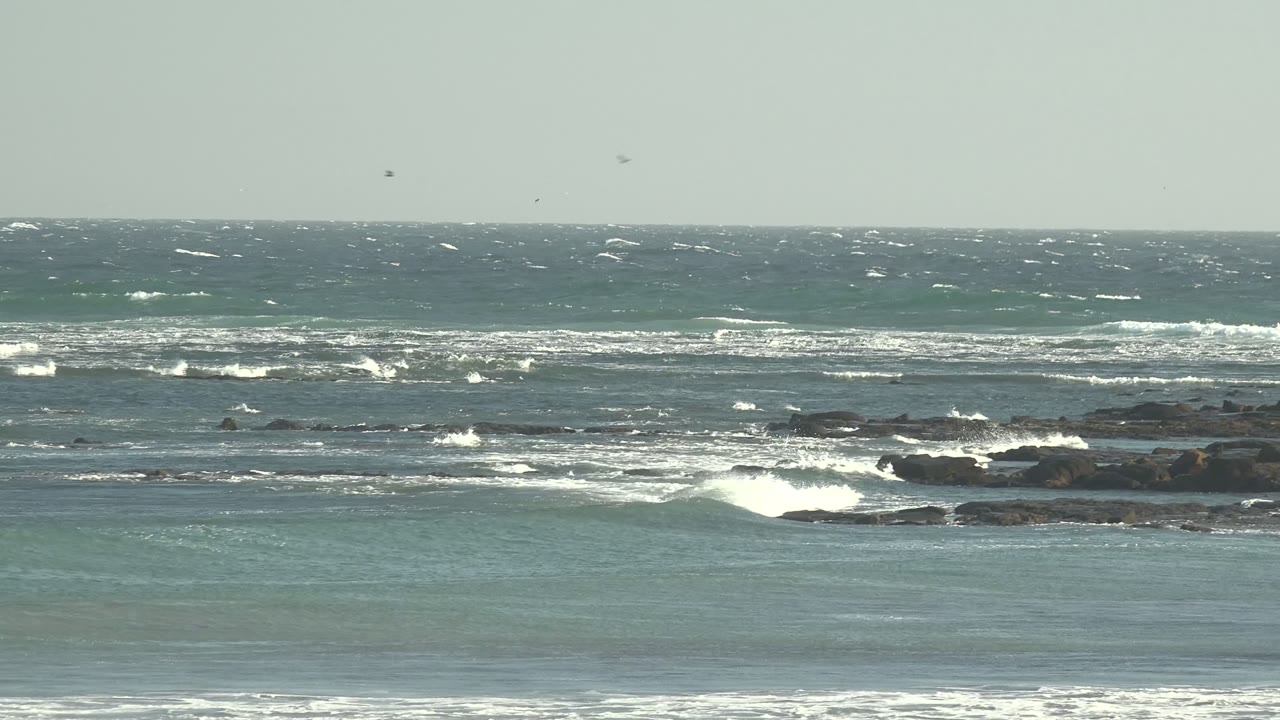 Whitecaps spread across offshore rocks with shallow water in front.