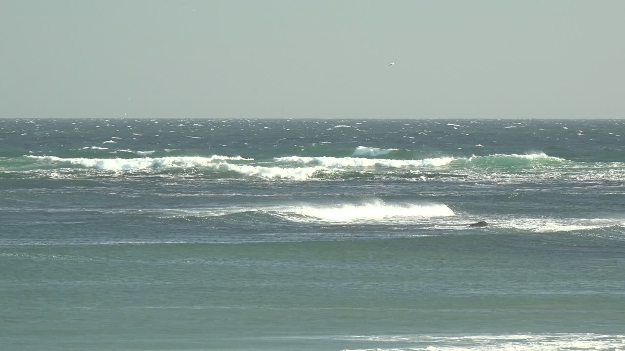 Wide view of blue-green ocean at La Bocana with layered whitecaps under a pale sky and no visible people.