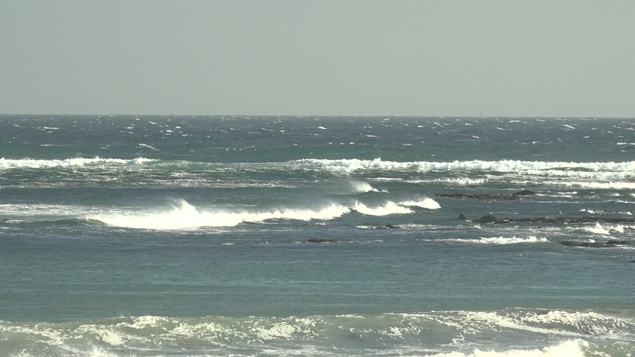 Layered blue-green water and foamy white surf stretch across La Bocana's rocky shoreline, with the horizon steady and no visible people.