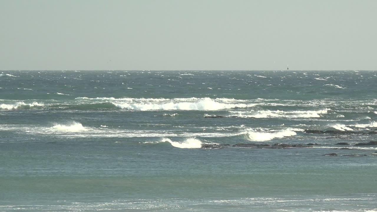 La Bocana surf with bright foam bands spreading over midground rocks, a flat horizon, and no visible people.