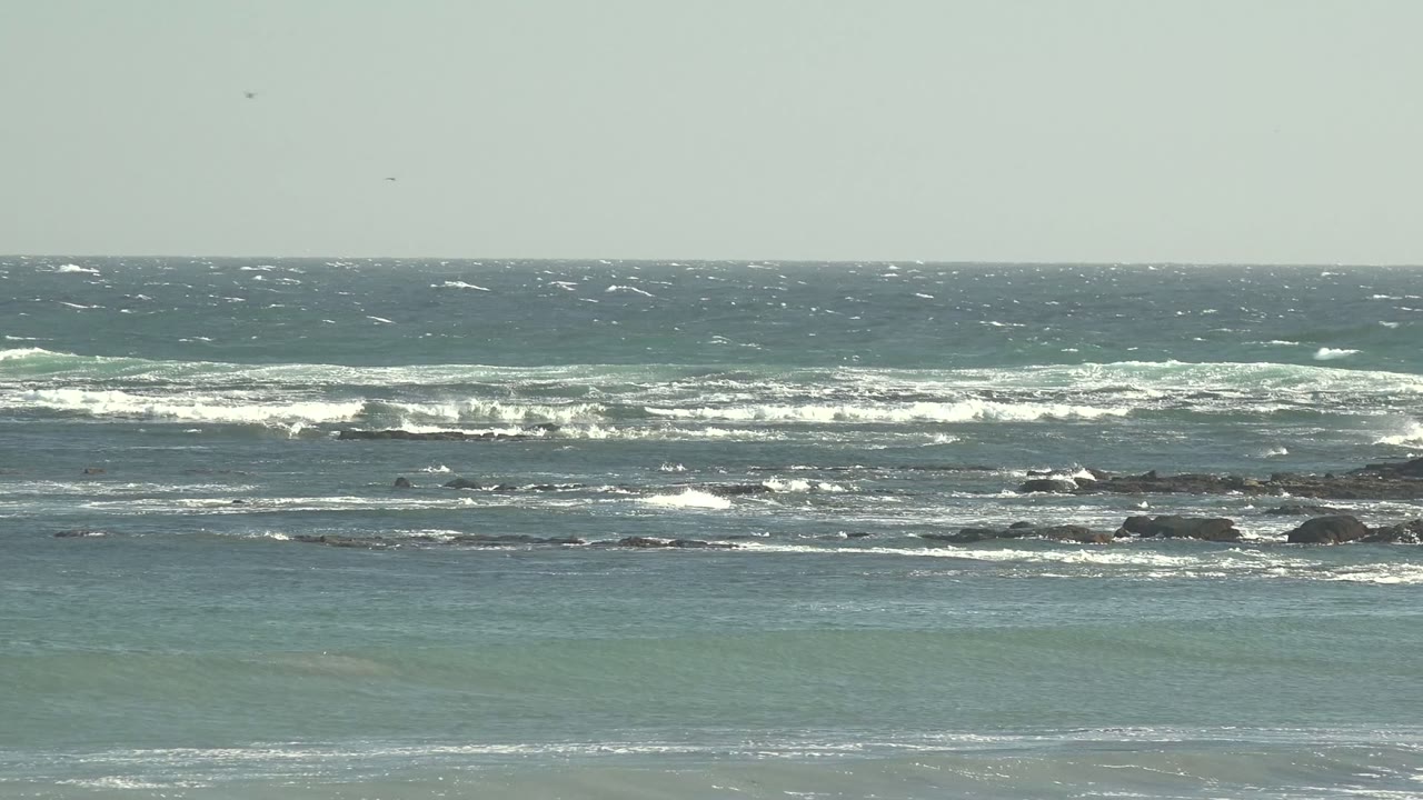 A choppy La Bocana ocean view shows white surf lines stepping toward dark offshore rocks and calmer green water near the bottom, no visible people.