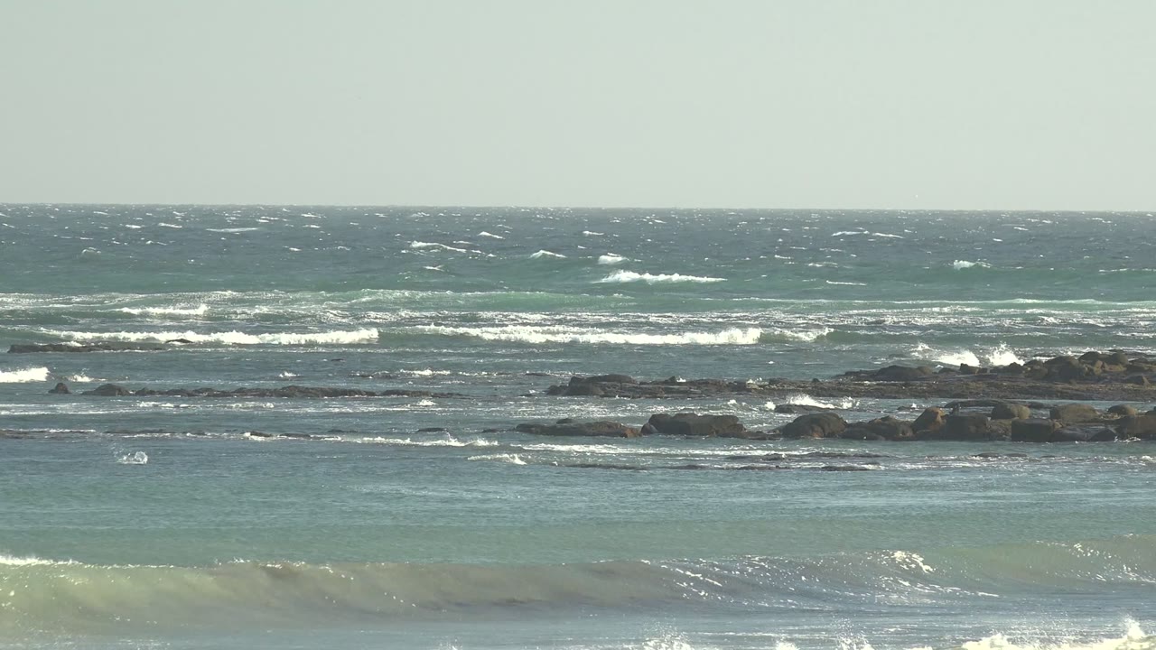 Wide view of La Bocana, Baja California Sur ocean surf with white foam breaking near rocky outcrops and no visible people.