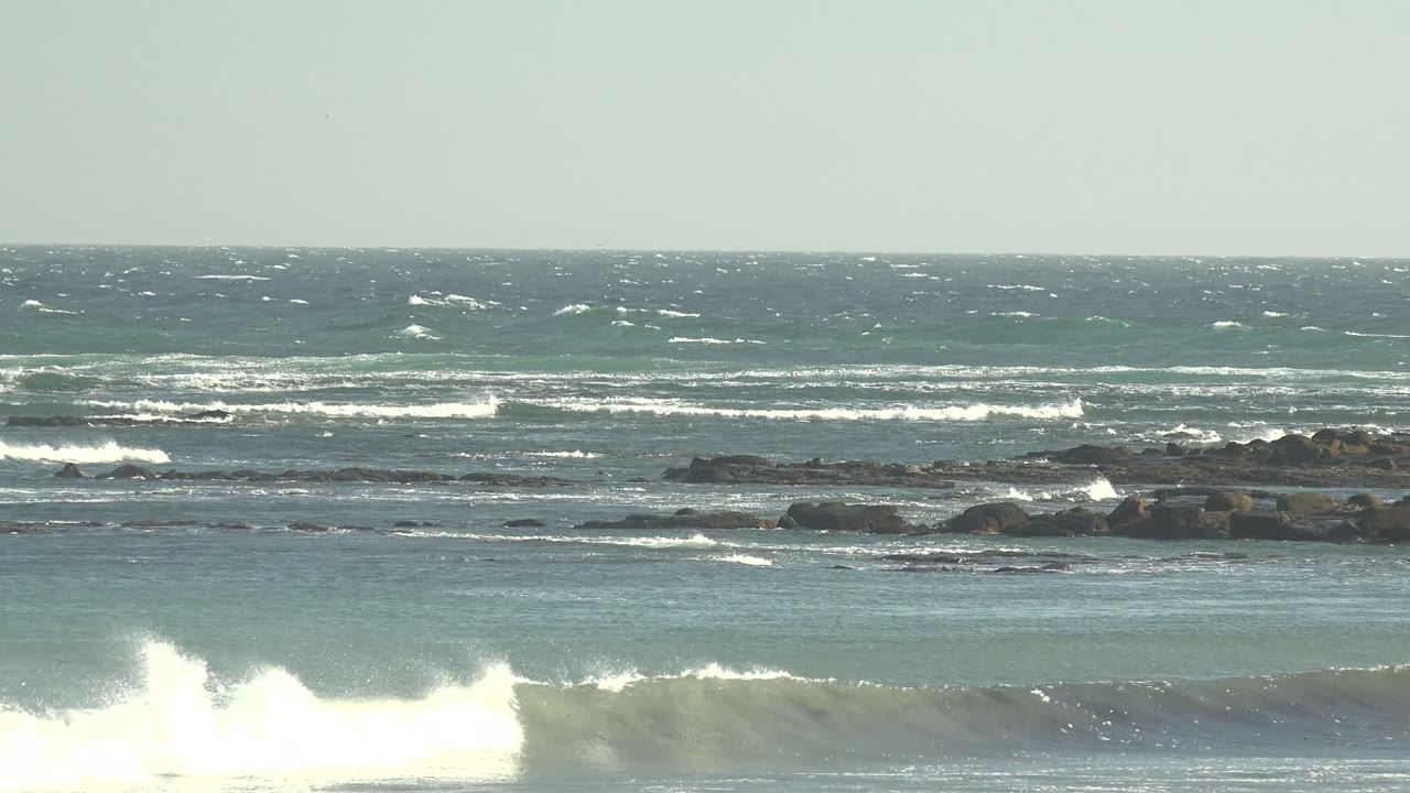 Wave crest throwing white spray near dark rocks