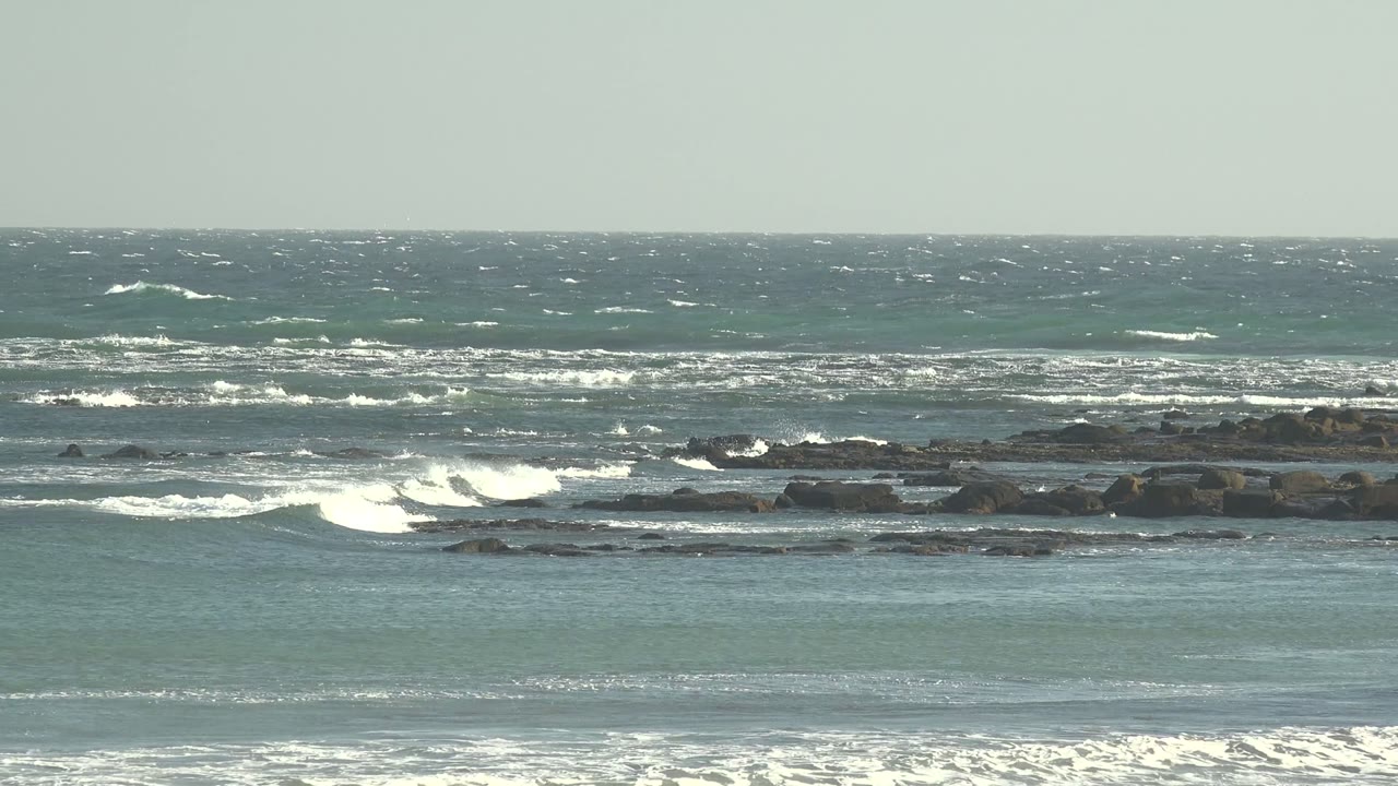 At two seconds, foamy water gathers near the foreground while whitecaps continue across the La Bocana horizon, with dark shoreline rocks and no visible people.