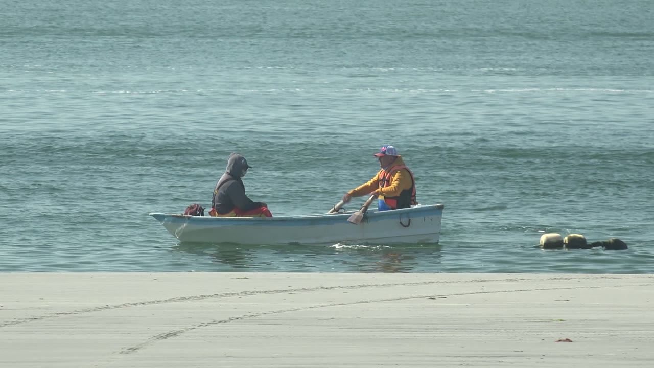 Small rowboat with two people beside calm blue-green water
