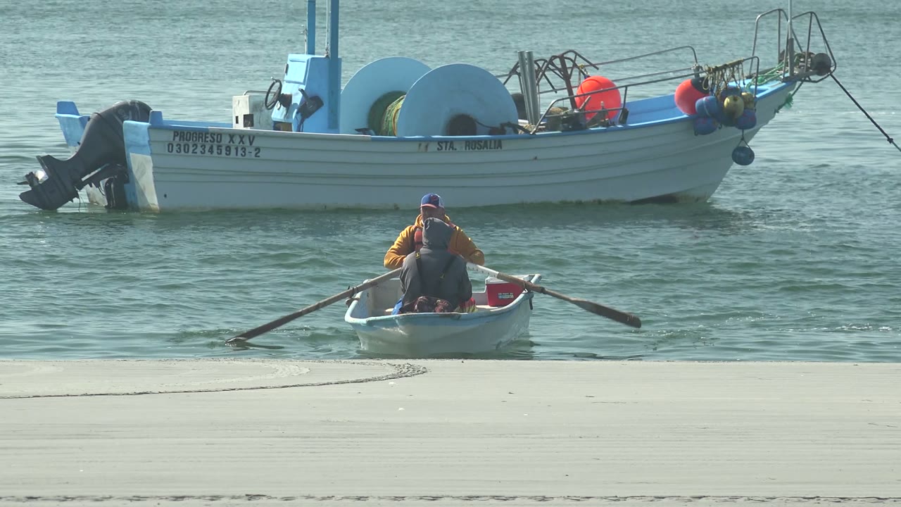 Small rowboat with two people moving in front of a larger boat.