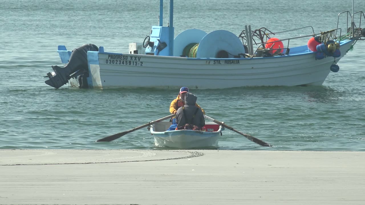 At 0:02 in La Bocana, the dinghy has shifted slightly right, with both oars extended over the water and the larger vessel remaining behind it.