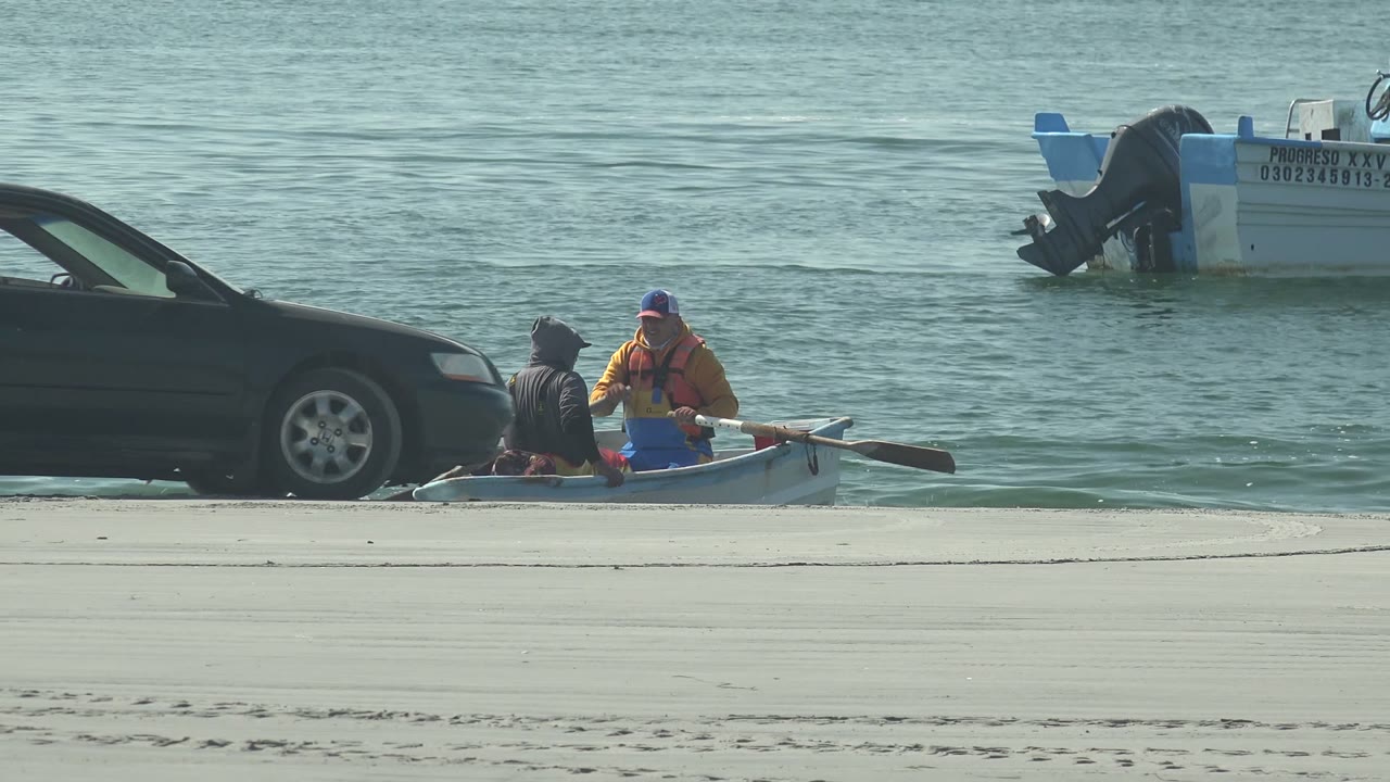 Car moving beside a small boat with two people near the water