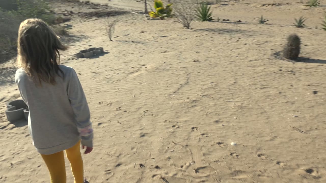 A rear view shows the girl farther into the sandy San Carlos desert terrain, with cactus, small shrubs, and footprints visible around her.