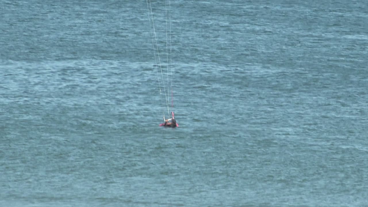 A distant kite surfer in San Juanico, Mexico sits low in blue ocean water with thin kite lines rising out of frame.