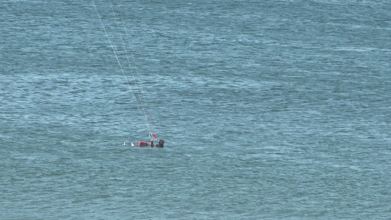 Kite surfer partly raised on the water with a small board wake.