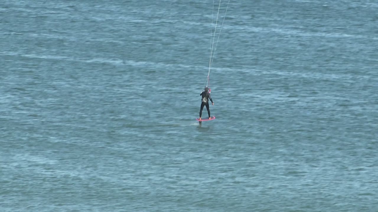 Kite surfer centered over calm blue water with kite lines above.