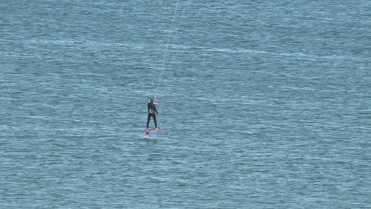 Kiteboarder centered on open blue water with kite lines above.