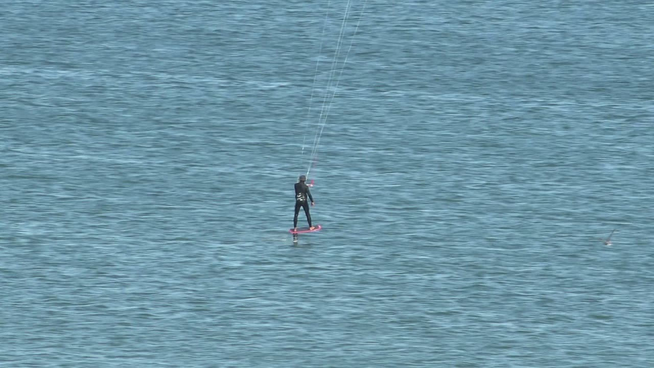 At 0:02, the kiteboarder remains distant on San Juanico ocean water, with the red board and upright body silhouetted against blue ripples.