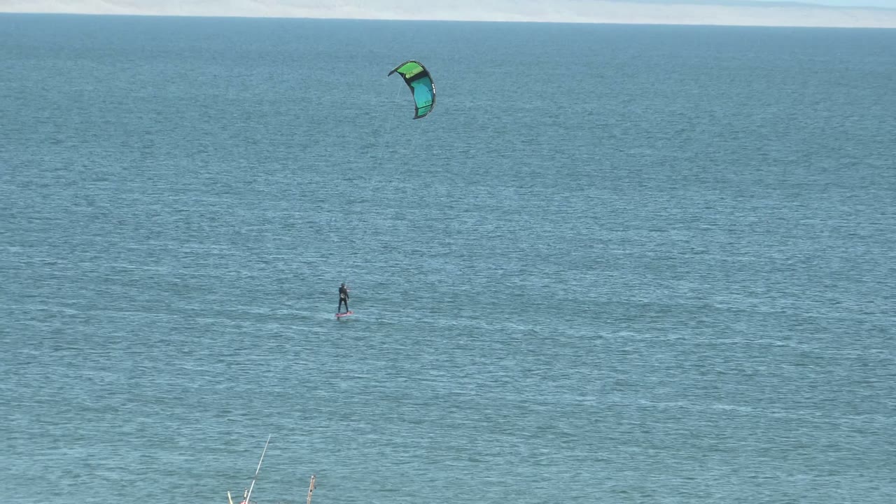 Kite surfer continues across calm blue water with kite overhead.